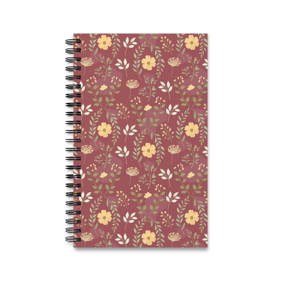 A spiral-bound notebook with a dusty rose cover decorated with a repeating floral pattern of yellow flowers and green leaves, shown on a plain white background.