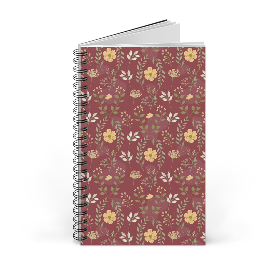 A spiral-bound notebook with a dusty rose cover decorated with a repeating pattern of yellow flowers, green leaves, and small botanical details, shown on a clean white background.
