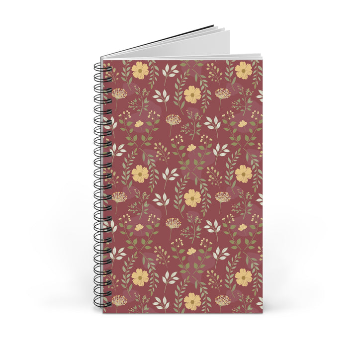 A spiral-bound notebook with a dusty rose cover decorated with a repeating pattern of yellow flowers, green leaves, and small botanical details, shown on a clean white background.