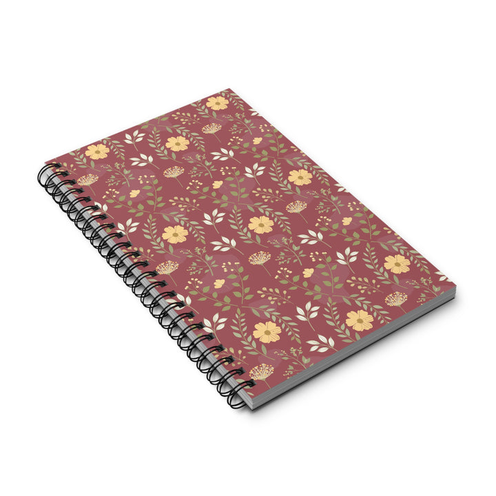 A spiral-bound notebook with a dusty rose cover decorated with a delicate floral pattern of yellow and white flowers and green leaves, shown on a clean white background.