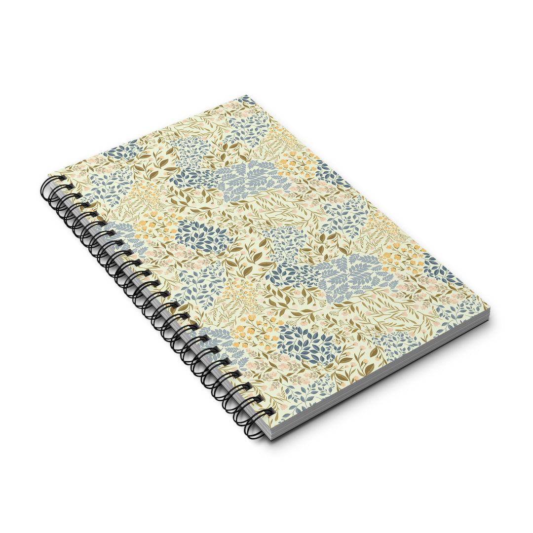A spiral-bound notebook with a cream-colored cover decorated in a botanical pattern of blue and olive-green leaves, shown on a clean white background.