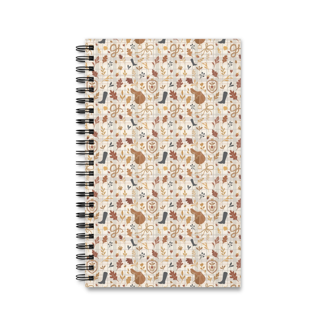 A spiral-bound notebook with a cream-colored cover featuring a repeating autumn-themed pattern of brown leaves, acorns, musical instruments, and birds, shown on a plain white background.