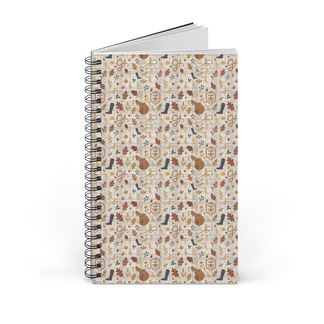 A spiral-bound notebook with a cream-colored cover decorated with a repeating pattern of autumn-themed illustrations, including leaves, birds, and animals in brown, orange, and blue tones. The notebook is shown standing upright on a clean white background.