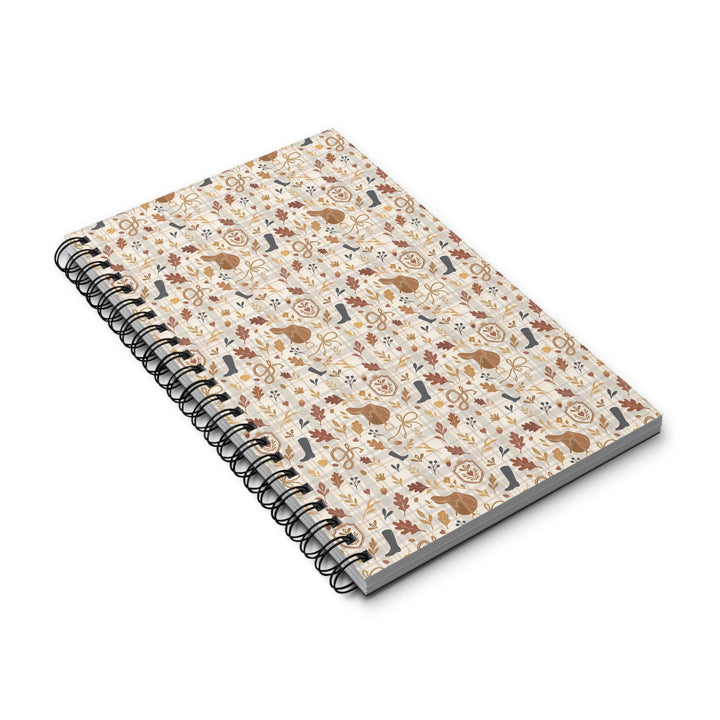 A spiral-bound notebook with a cream-colored cover decorated with a dense pattern of brown rabbits, leaves, and small floral motifs, shown on a plain white background.