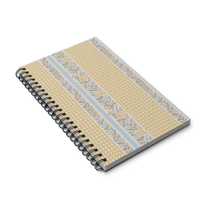 A spiral-bound notebook with a cream and beige floral patterned cover, featuring light blue stripes and yellow floral accents, shown on a white background.