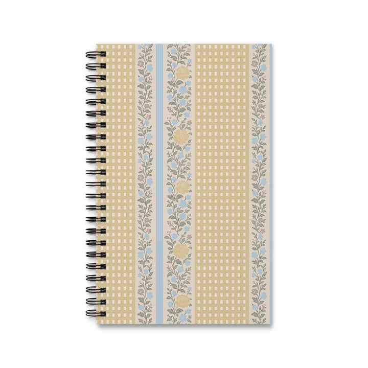 A spiral-bound notebook with a decorative cover featuring vertical stripes of beige gingham, floral patterns, and light blue accents, shown on a plain white background.