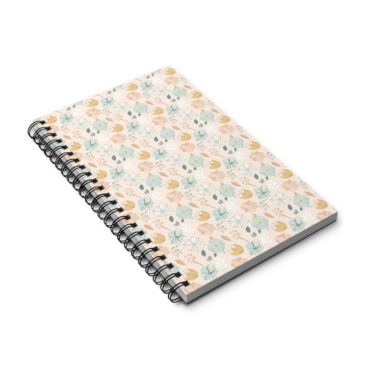 A spiral-bound notebook with a light cream cover decorated with a delicate pattern of small blue, green, and yellow flowers and leaves, shown on a clean white background.