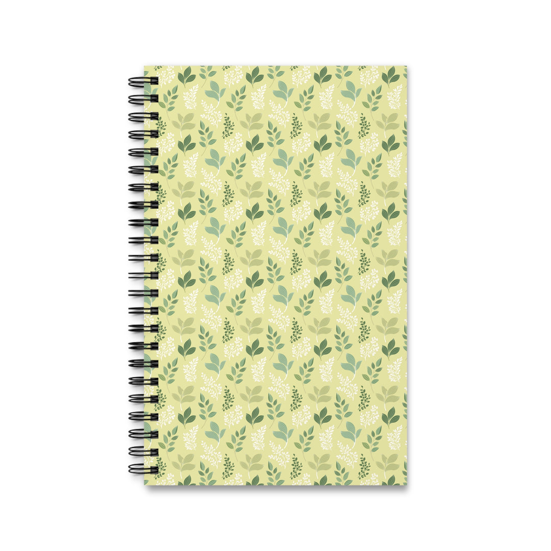 A spiral-bound notebook with a light yellow-green cover decorated with a repeating pattern of green leaves and botanical motifs, shown on a plain white background.