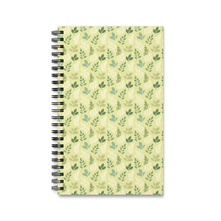 A spiral-bound notebook with a light yellow-green cover decorated with a repeating pattern of green leaves and botanical motifs, shown on a plain white background.