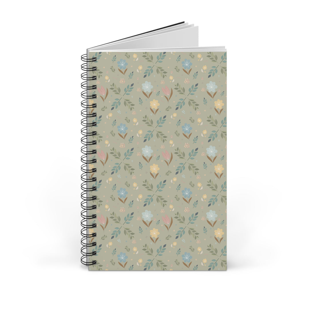 A spiral-bound notebook with a muted sage green cover decorated with a delicate repeating pattern of small flowers, leaves, and birds in soft pastel shades of blue, yellow, pink, and brown. The notebook is shown standing upright on a clean white background.