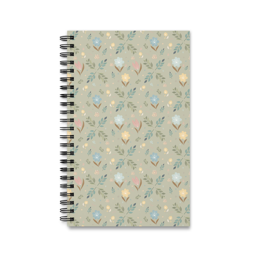 A spiral-bound notebook with a muted sage green cover featuring a delicate, repeating floral and leaf pattern in soft pastel shades of blue, yellow, pink, and green. The notebook is bound with a black metal spiral on the left side and is photographed against a clean white background.