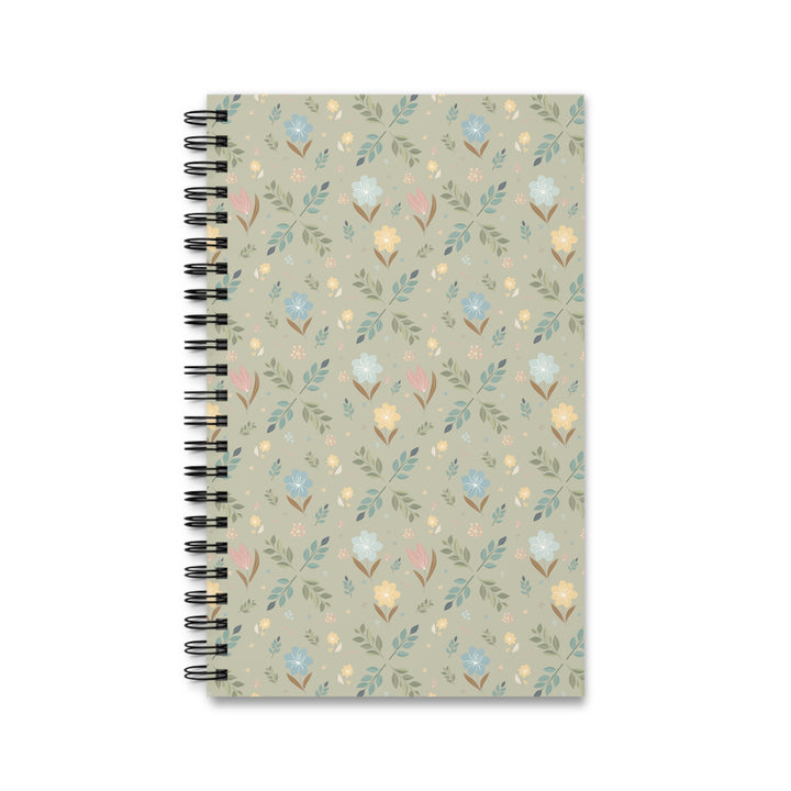A spiral-bound notebook with a muted sage green cover featuring a delicate, repeating floral and leaf pattern in soft pastel shades of blue, yellow, pink, and green. The notebook is bound with a black metal spiral on the left side and is photographed against a clean white background.