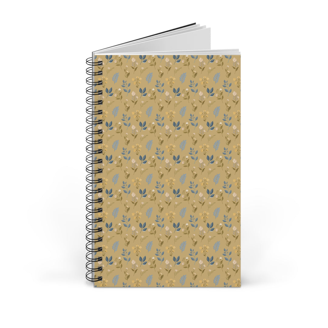 A spiral-bound notebook with a tan cover featuring a repeating pattern of small blue and white leaves, shown on a clean white background.