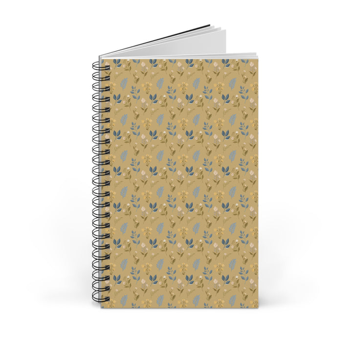 A spiral-bound notebook with a tan cover featuring a repeating pattern of small blue and white leaves, shown on a clean white background.