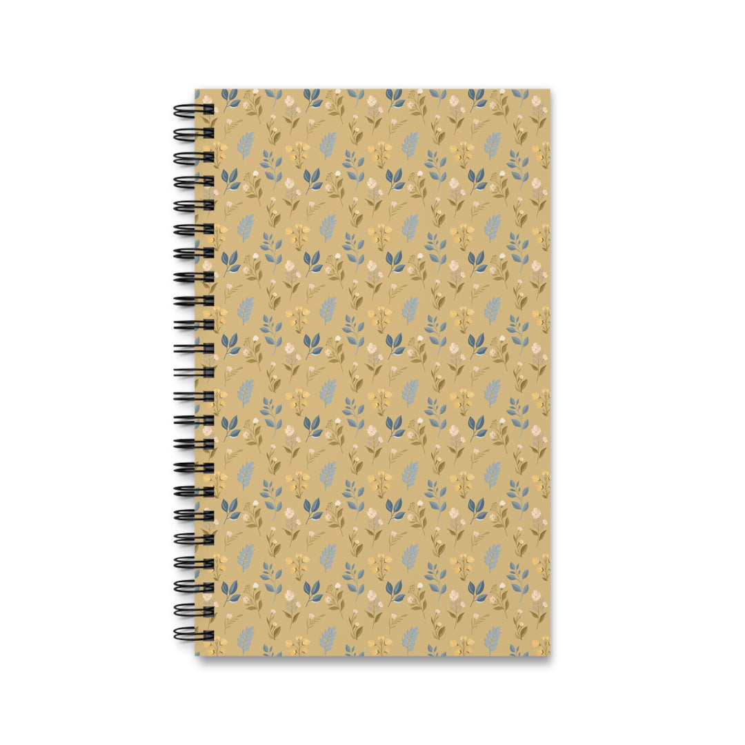 A spiral-bound notebook with a tan cover featuring a repeating pattern of small blue and yellow botanical illustrations, shown on a plain white background.