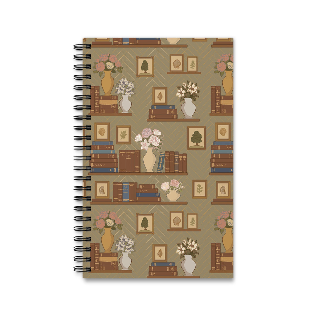 A spiral-bound notebook with a vintage-style bookshelf pattern on the cover, featuring brown books, vases with pink and white flowers, and framed art on a beige background.