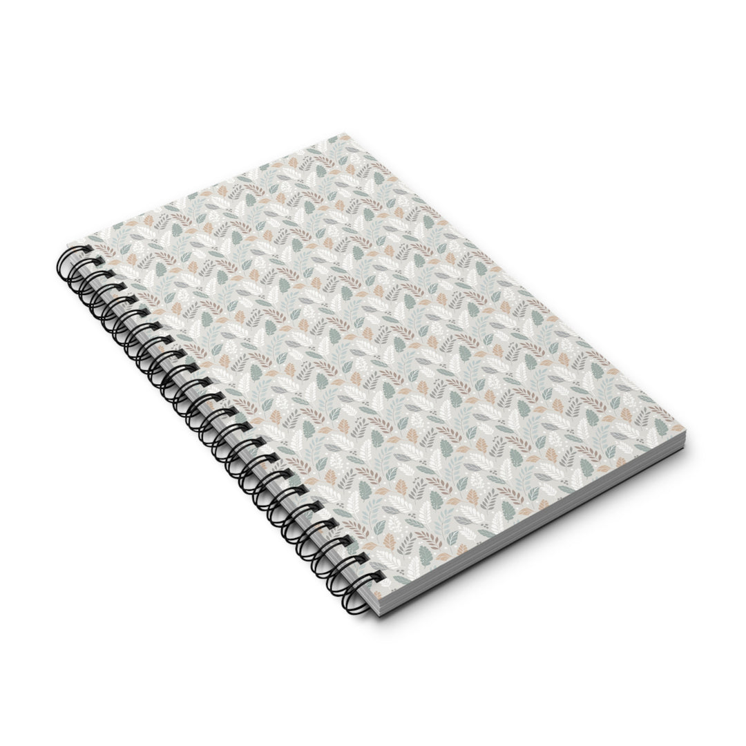 A spiral-bound notebook with a white cover decorated in a delicate, repeating botanical pattern of muted sage green leaves and soft peach flowers, bound with a black metal coil on a white background.
