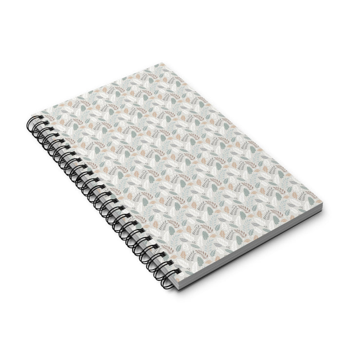 A spiral-bound notebook with a white cover decorated in a delicate, repeating botanical pattern of muted sage green leaves and soft peach flowers, bound with a black metal coil on a white background.