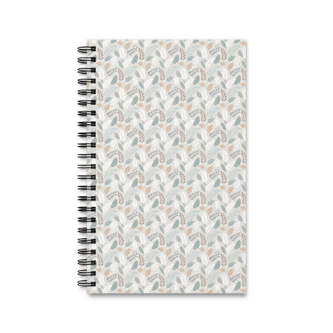 A spiral-bound notebook with a white cover decorated in a repeating pattern of muted sage green, dusty pink, and gray botanical leaves, shown on a plain white background.