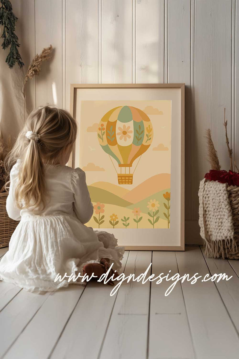 Child in a white dress sitting on the floor looking at a framed illustration of a hot air balloon.