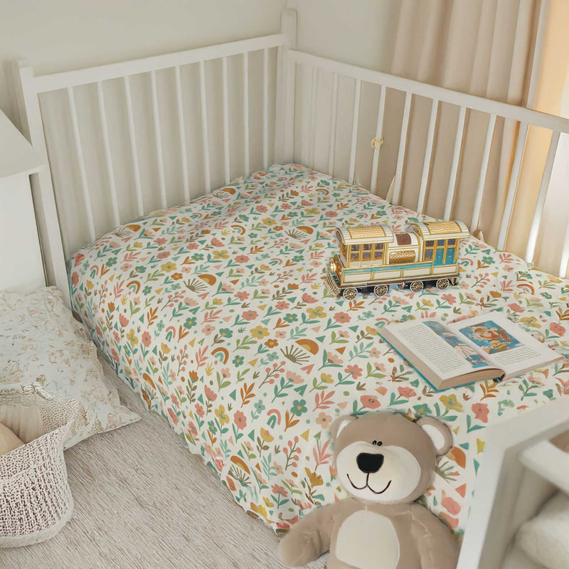 Children's crib with floral bedding, teddy bear, and toy train in a nursery setting.