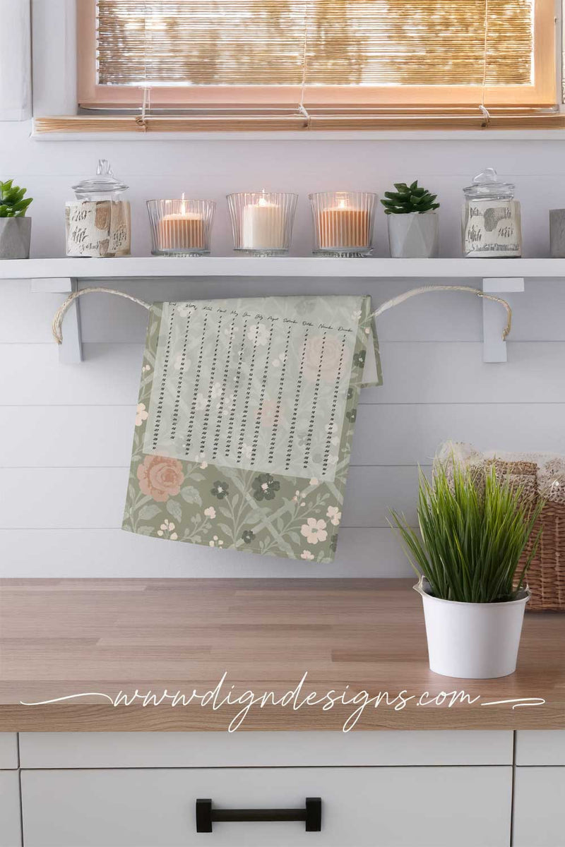Decorative towel with floral pattern hanging on a wooden shelf with candles and plants.