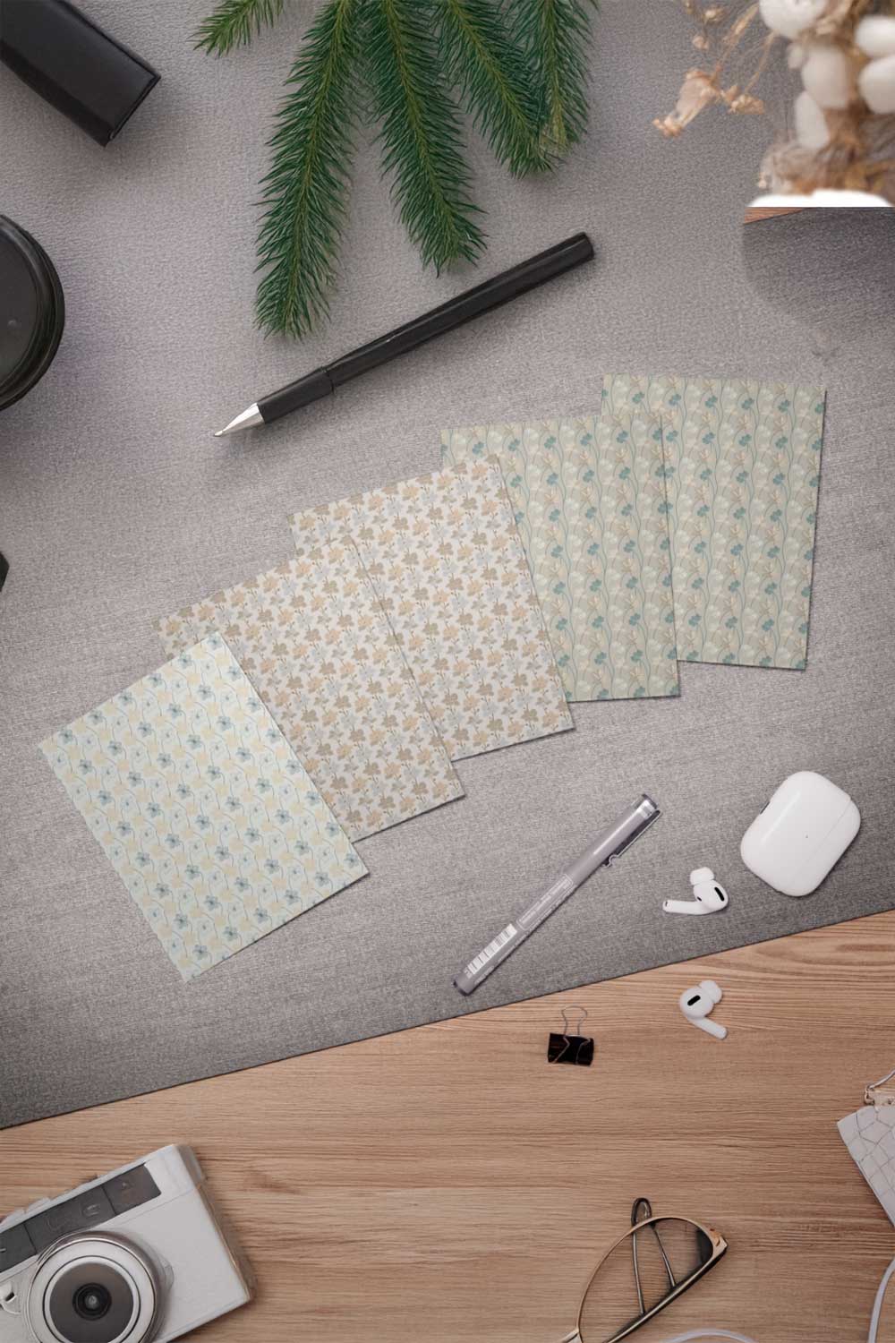 Desk with patterned paper sheets, a pen, camera, and other office supplies on a gray surface.