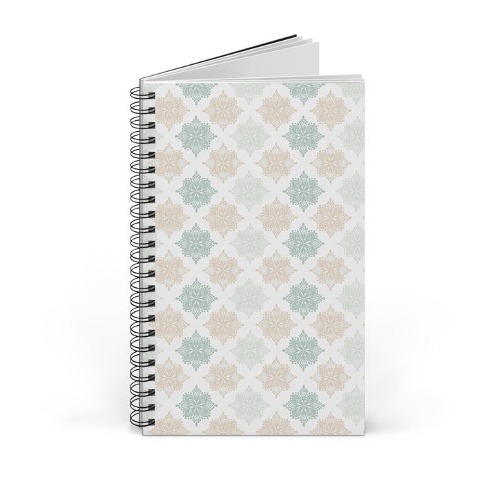 A spiral-bound notebook with a white cover featuring a repeating geometric pattern in soft sage green, dusty pink, and beige, shown on a clean white background.