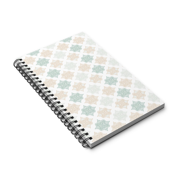 A spiral-bound notebook with a white cover featuring a repeating geometric lattice pattern in soft sage green and beige, shown on a clean white background.