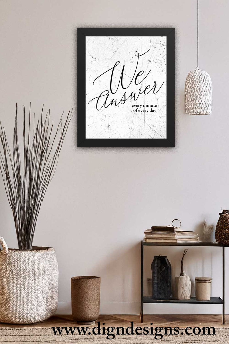 Framed artwork with 'We Answer every minute of every day' text on a white wall with decor items below. black