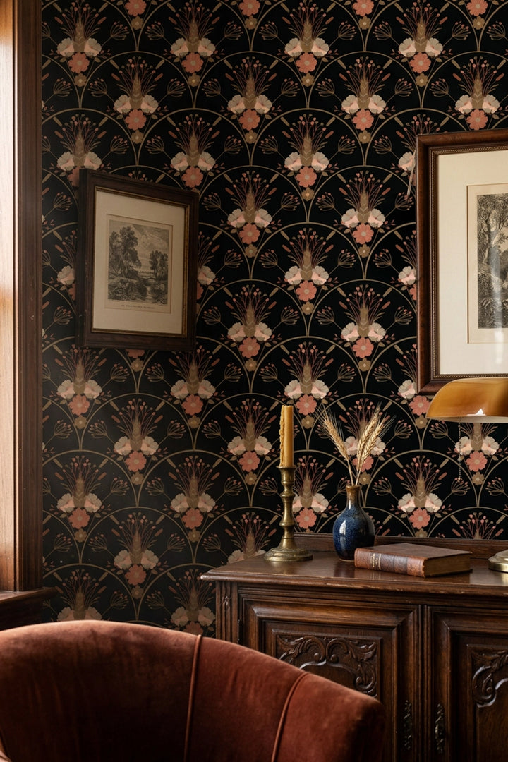 Dark wallpaper with a repeating Art Deco fan and floral pattern in black, gold, and dusty pink, shown in a styled room setting with a wooden console table, framed art, and a brown velvet chair.