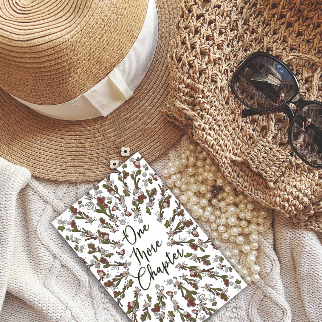 A bookmark with the words "one more chapter" written on it with flowers surrounding it 