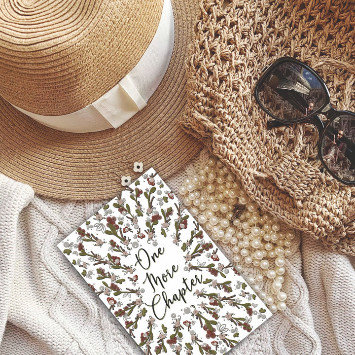 A bookmark with the words "one more chapter" written on it with flowers surrounding it 