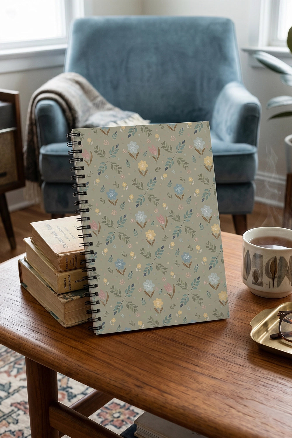 Notebook with decorative cover on a wooden table with books and a cup in a cozy room.