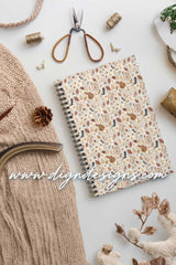 Notebook with floral pattern surrounded by knitting materials on a light background