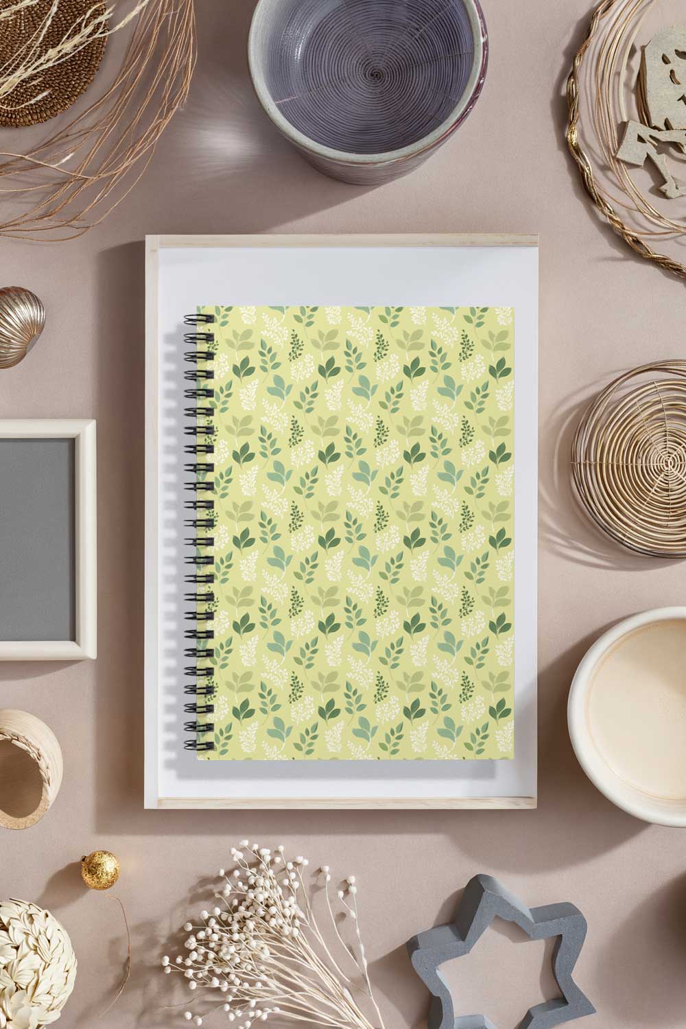 Notebook with green leaf pattern on a decorative surface with bowls and frames.