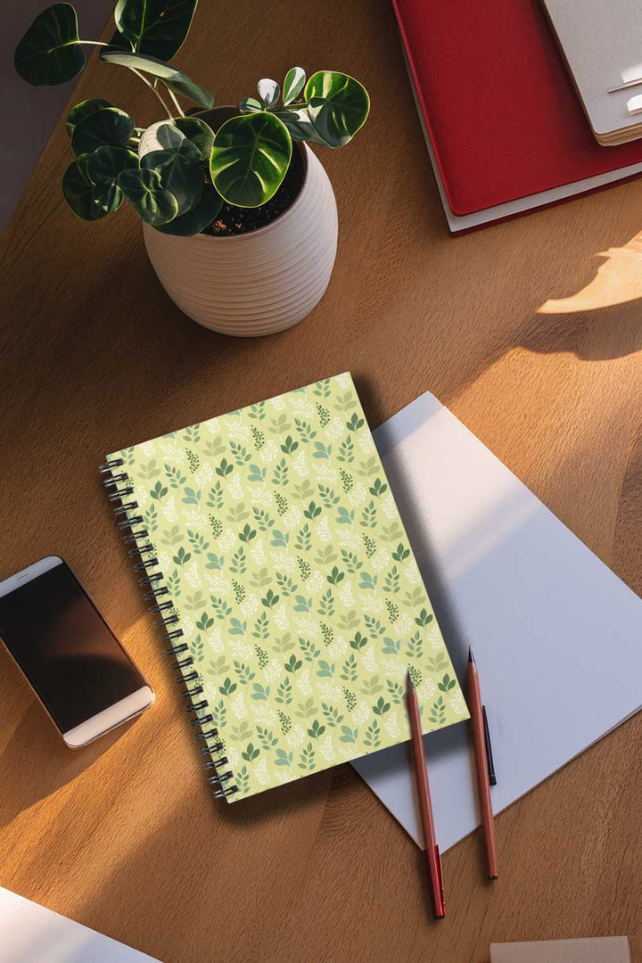 Notebook with green leaf pattern on a wooden desk with a plant and smartphone.