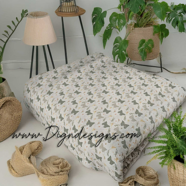 Patterned blanket on a bed with plants and decor in the background, featuring the brand &