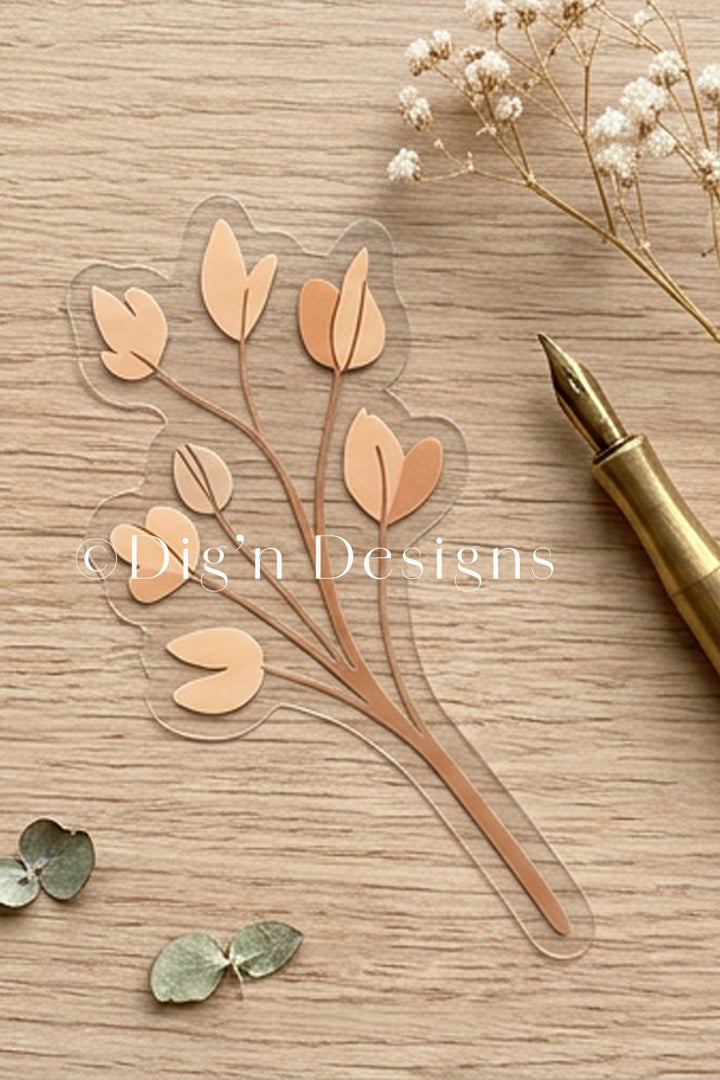 Transparent leaf-shaped cutting dies on a wooden surface with a pen and small flowers.