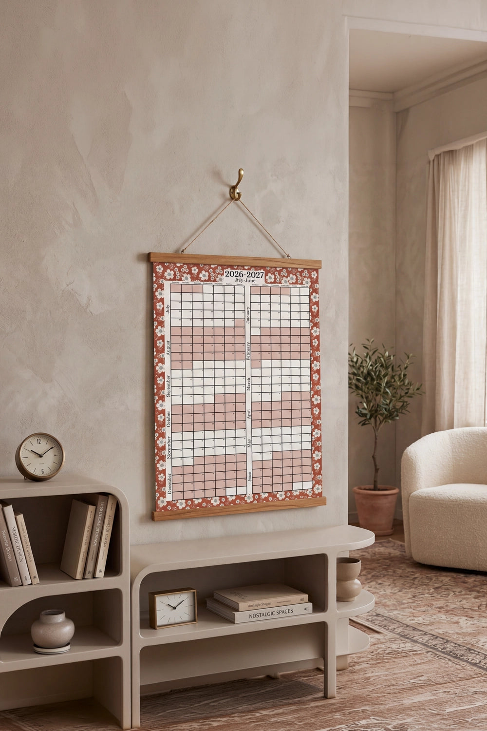 Wall calendar with floral border hanging on a wall in a room with a bookshelf and clock.
