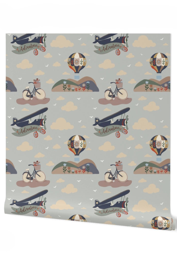 A roll of wallpaper featuring a whimsical vintage pattern with biplanes, hot air balloons, bicycles, clouds, and small illustrated figures on a light gray background.