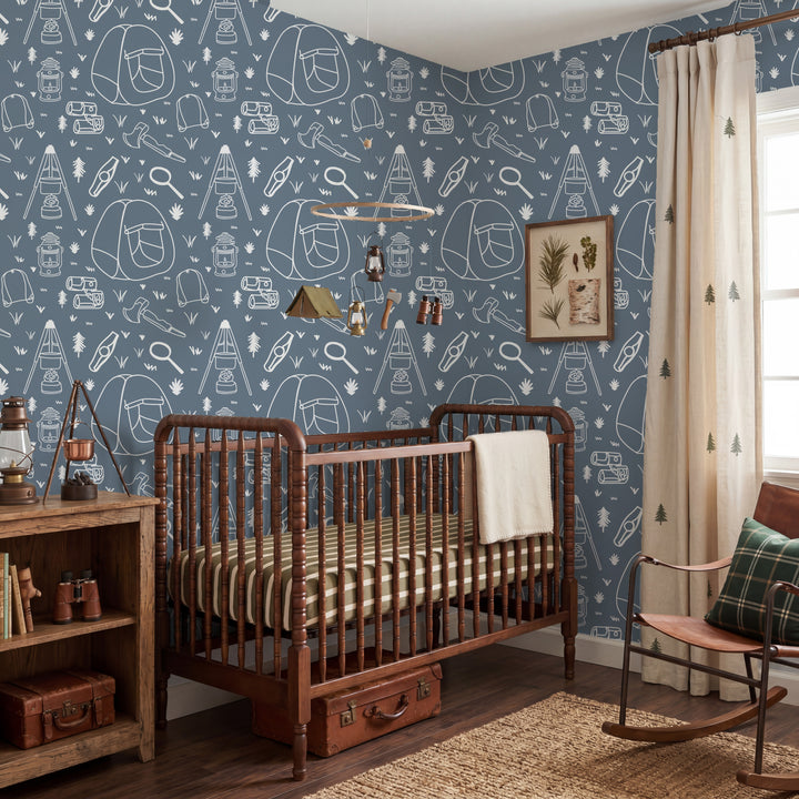 A styled nursery room featuring blue wallpaper with white camping-themed line drawings, a wooden crib with striped bedding, a rustic wooden shelf, and a rocking chair by a window.