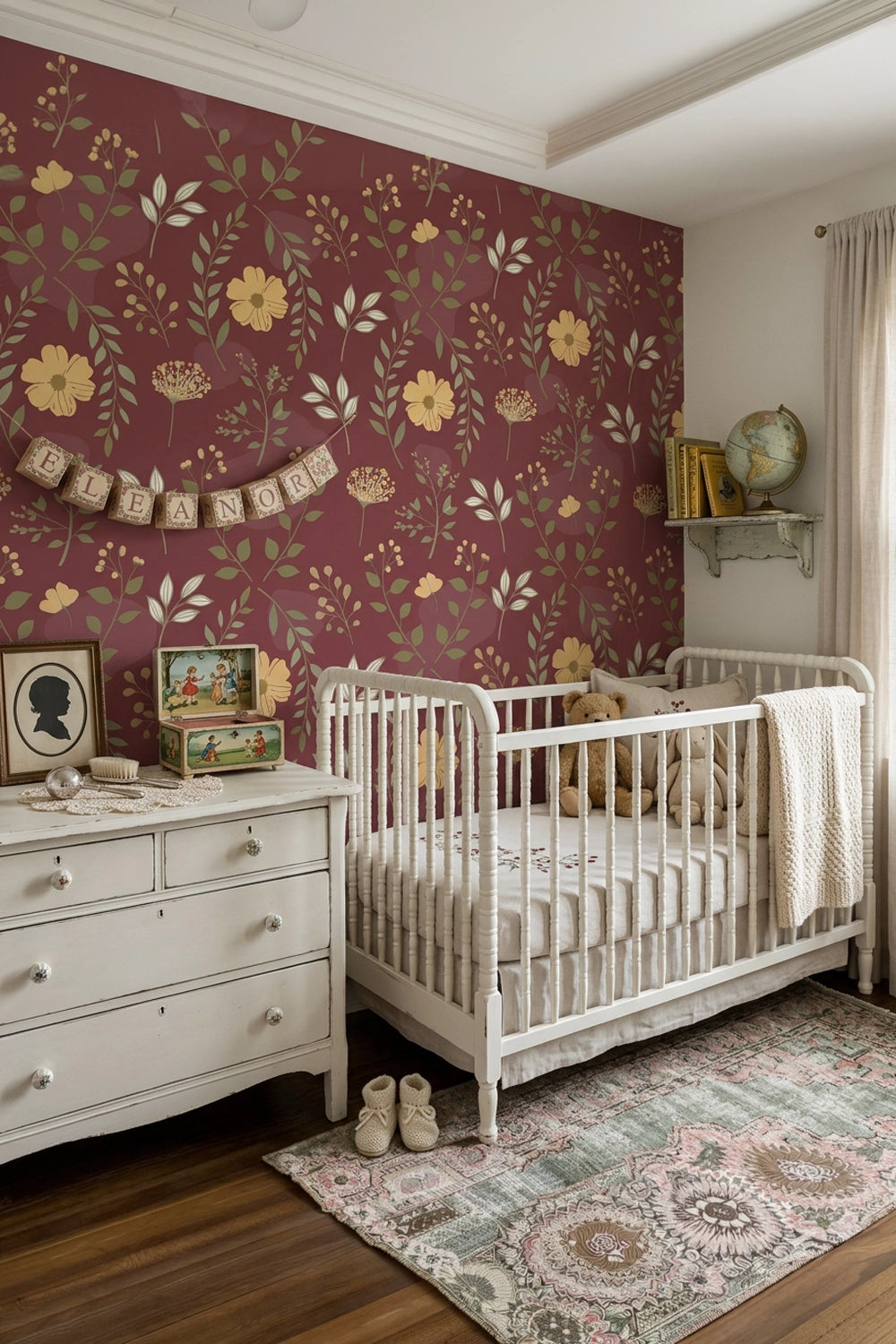 A styled nursery room featuring a prominent burgundy floral wallpaper on the main wall, a white wooden crib, a matching white dresser, and a patterned rug on a dark wood floor.