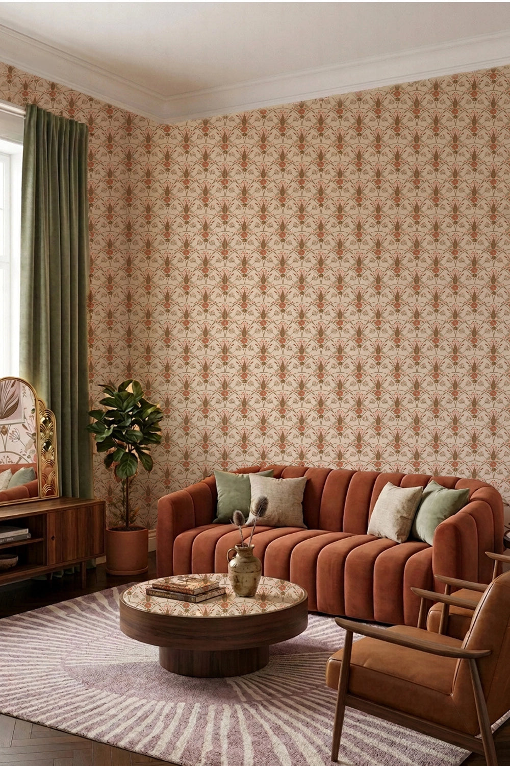 A styled living room corner featuring a wall covered in a repeating brown and beige floral patterned wallpaper. The room is furnished with a rust-orange velvet sofa, a matching armchair, a round wooden coffee table, a striped rug, and a green curtain by a window.