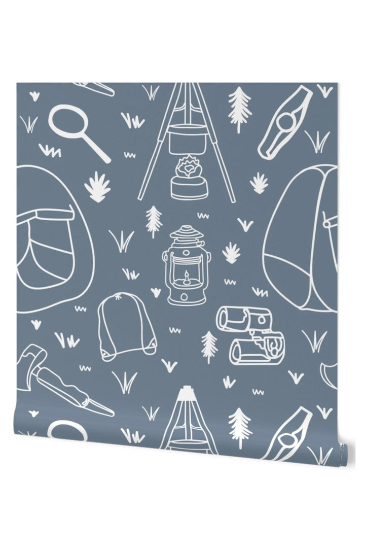 A roll of wallpaper featuring a muted slate blue background with a white line-art pattern of outdoor camping gear, including tents, lanterns, trees, and backpacks.