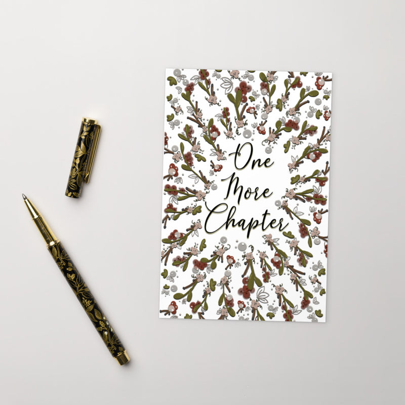 A bookmark with the words "one more chapter" written on it with flowers surrounding it 