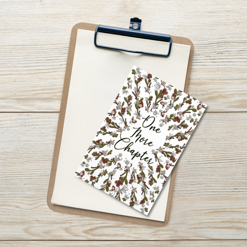 A bookmark with the words "one more chapter" written on it with flowers surrounding it 