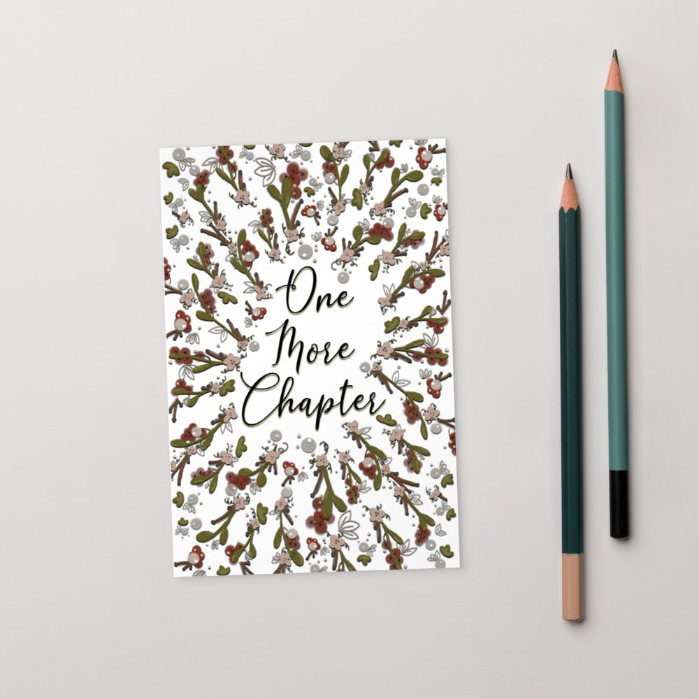 A bookmark with the words "one more chapter" written on it with flowers surrounding it 