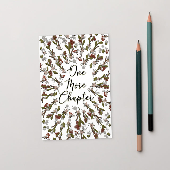 A bookmark with the words "one more chapter" written on it with flowers surrounding it 