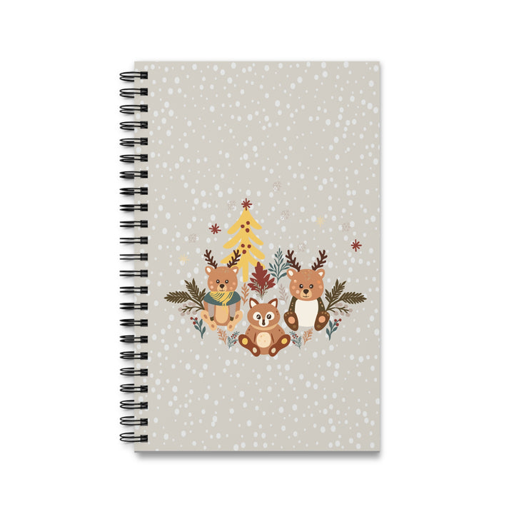 A spiral-bound notebook with a festive winter cover design featuring three woodland animals, a Christmas tree, and snowflakes on a light gray background.